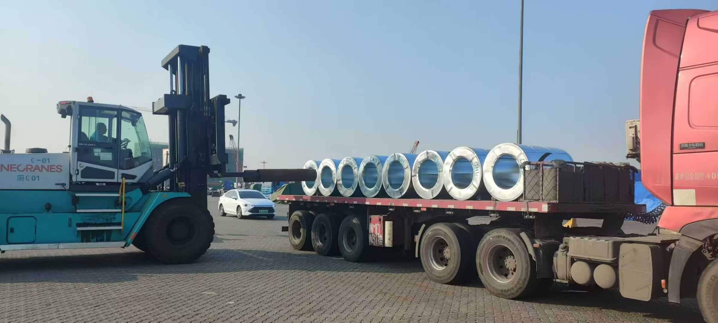 Coil-handling forklift beside a truck carrying CNU-marked wrapped coils