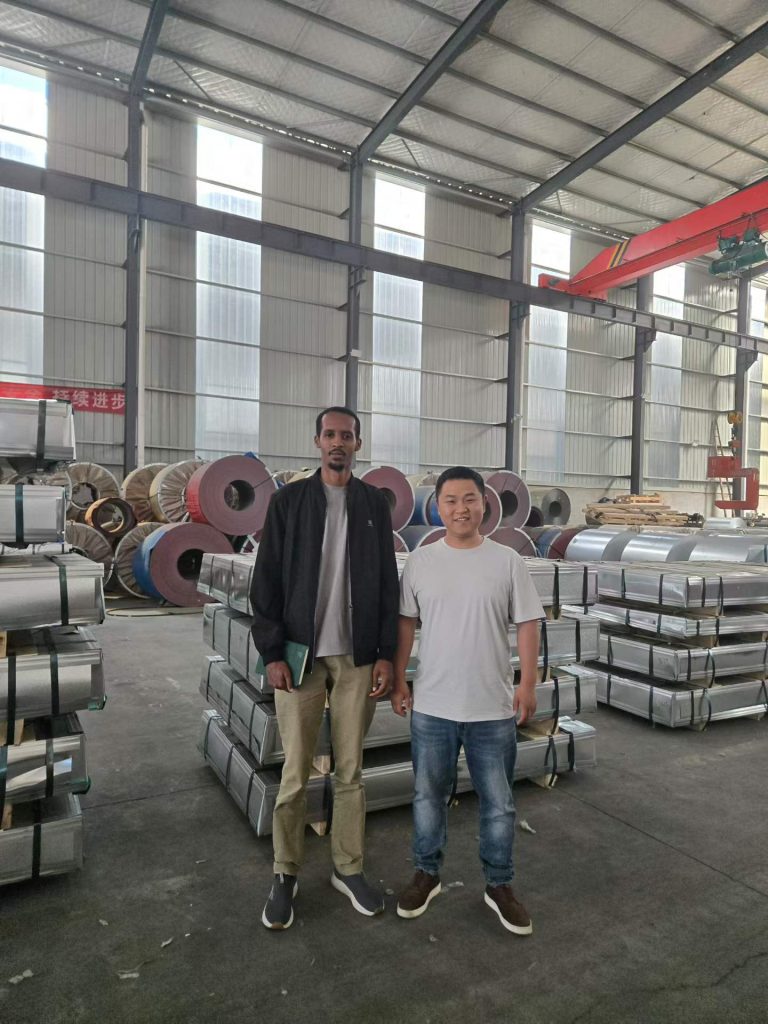 Visitors in the factory warehouse alongside packed sheets and coils.